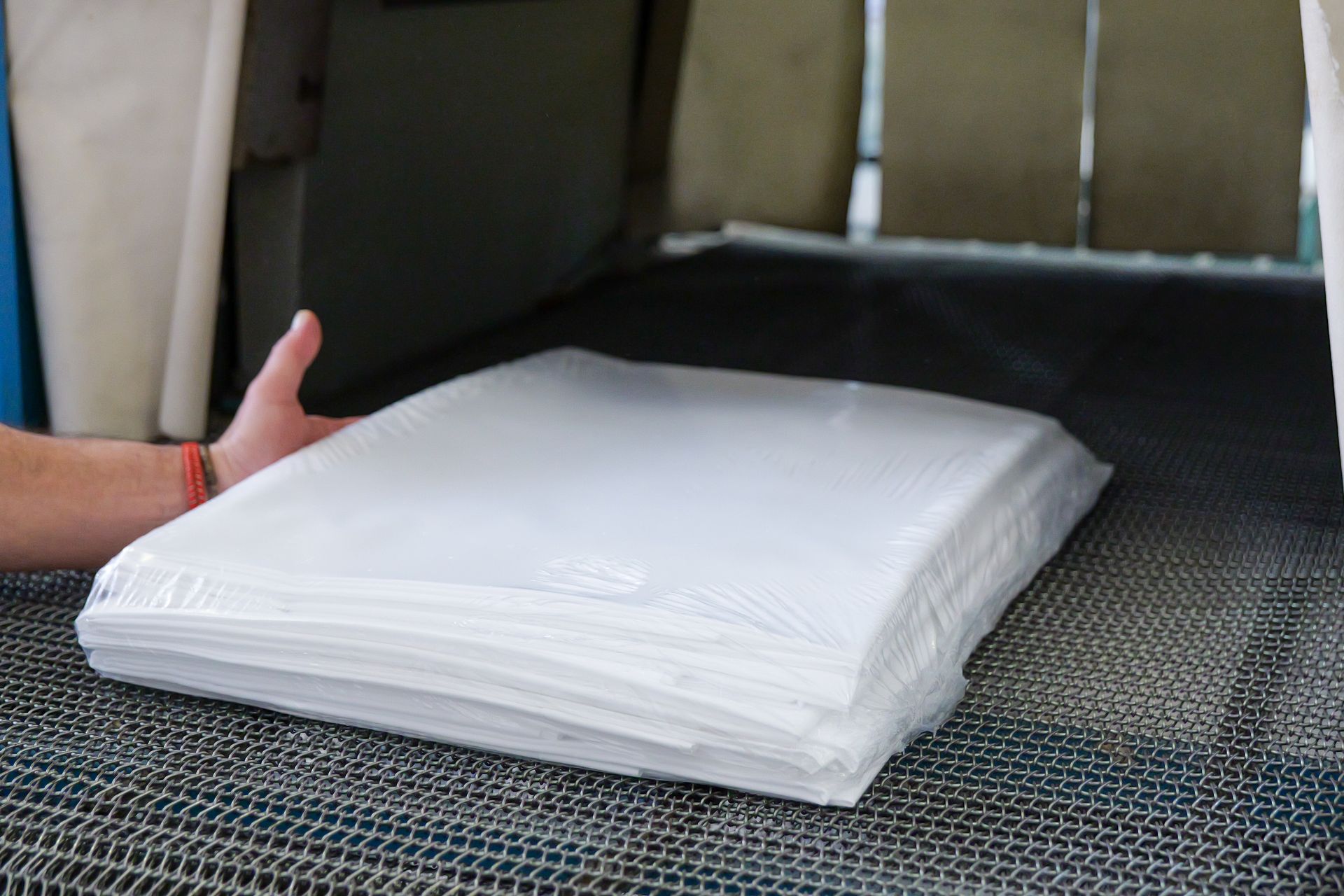 Posizionamento manuale di un tampone bianco piegato su un nastro trasportatore intrecciato.