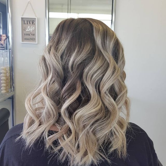 A Woman With Long Wavy Blonde Hair is Sitting in Front of a Mirror — Lush Hair Studio in Tumbi Umbi, NSW
