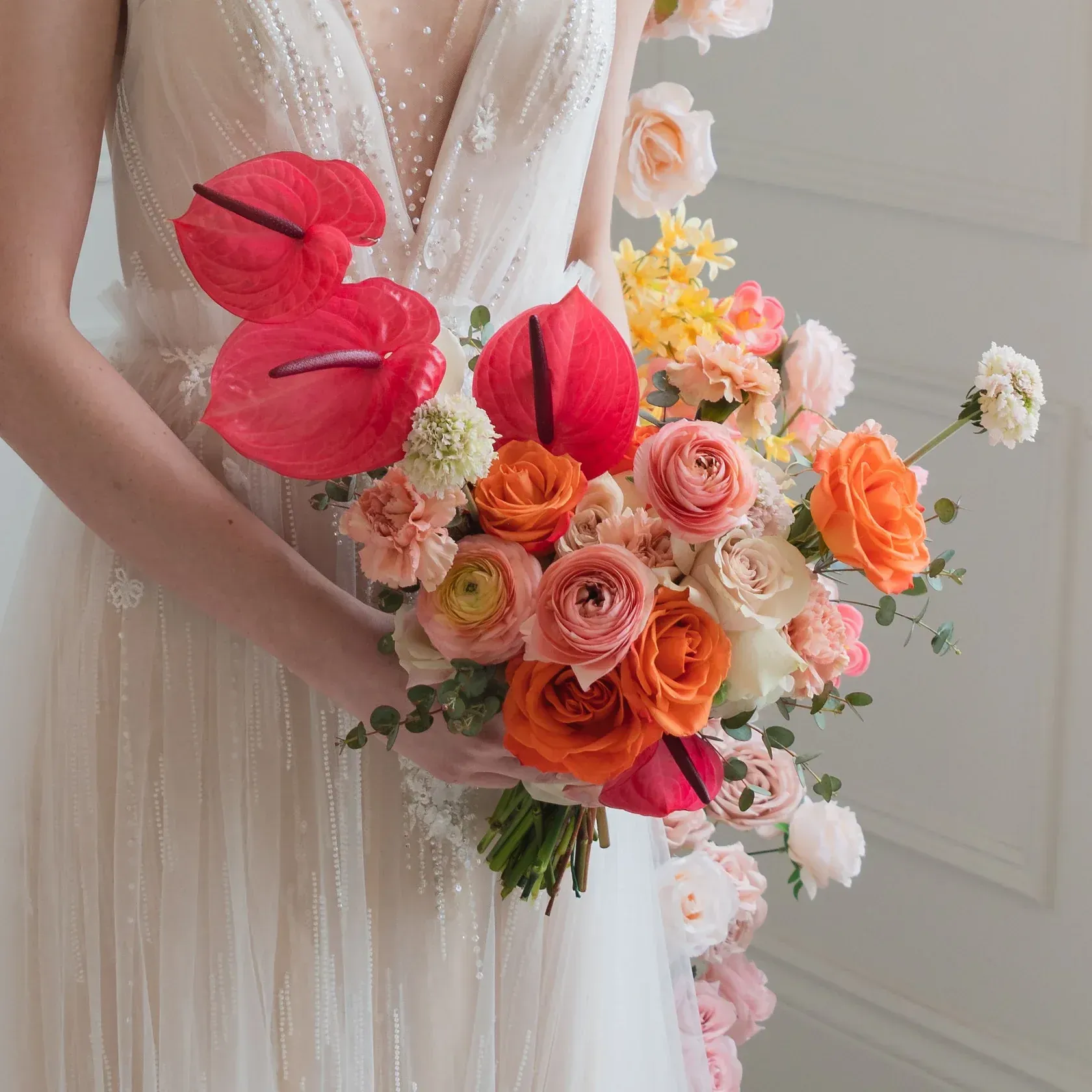 Bride in white dress holding colorful bouquet with orange and pink flowers.