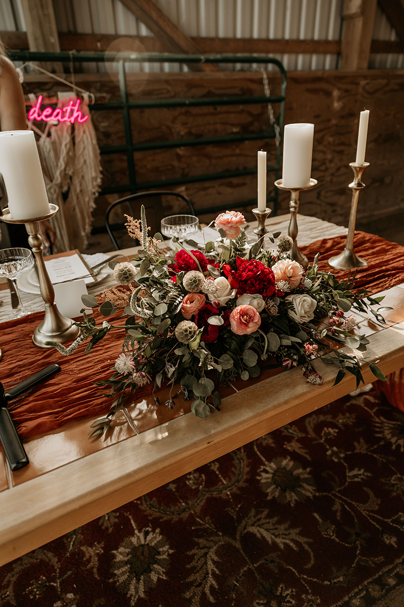 A wedding reception table featuring a floral centerpiece, candles, and a neon