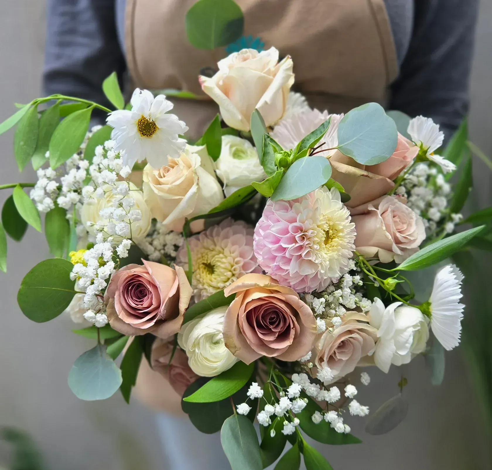 Person holding a bouquet of light-colored roses, daisies, and other flowers with greenery.