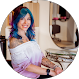 Woman with blue hair and tattoos smiles, wearing an off-the-shoulder white top. She is indoors.