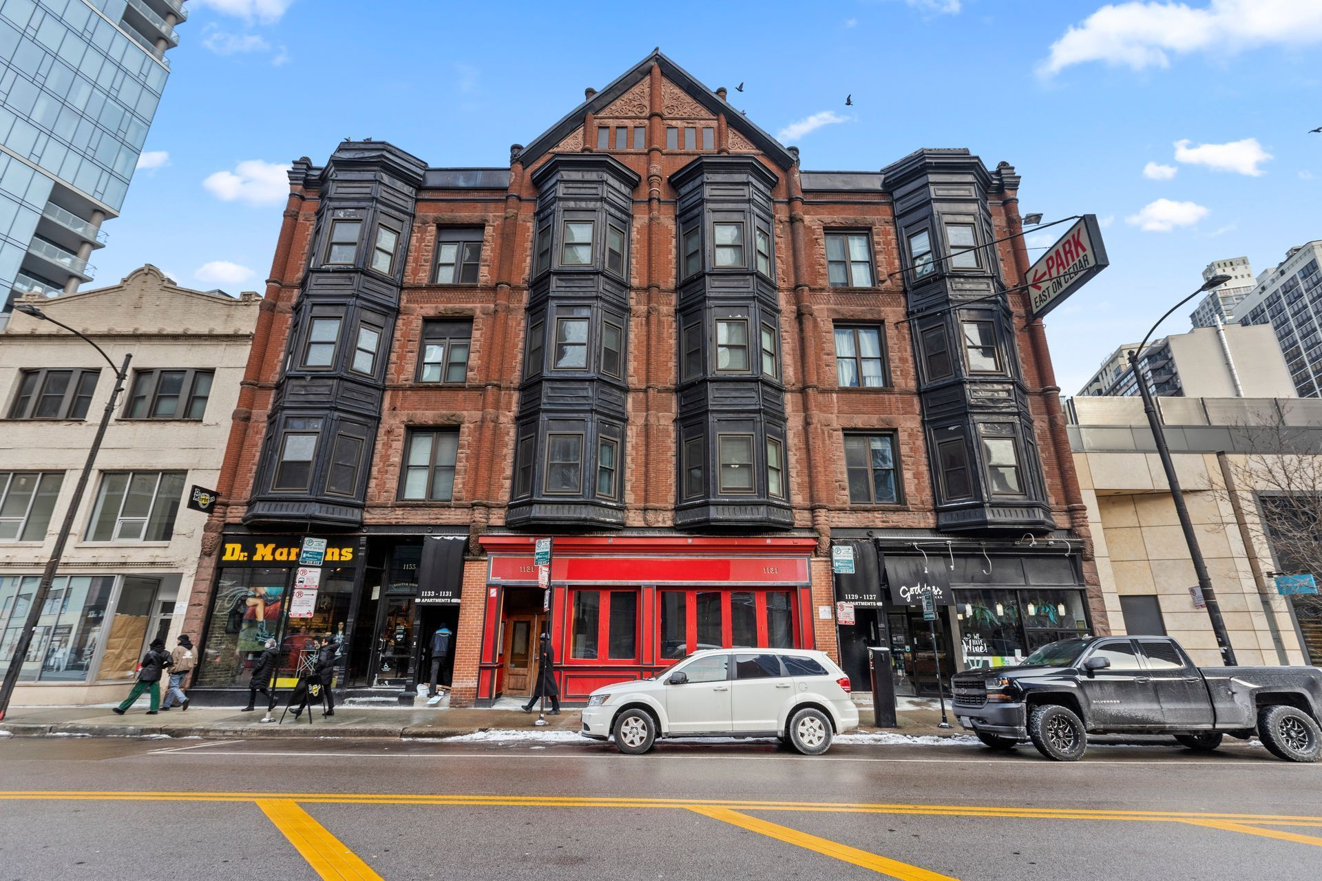 A white car is parked in front of a large brick building.