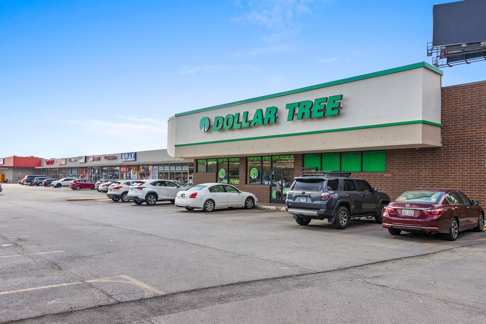 A row of cars are parked in front of a dollar tree store.