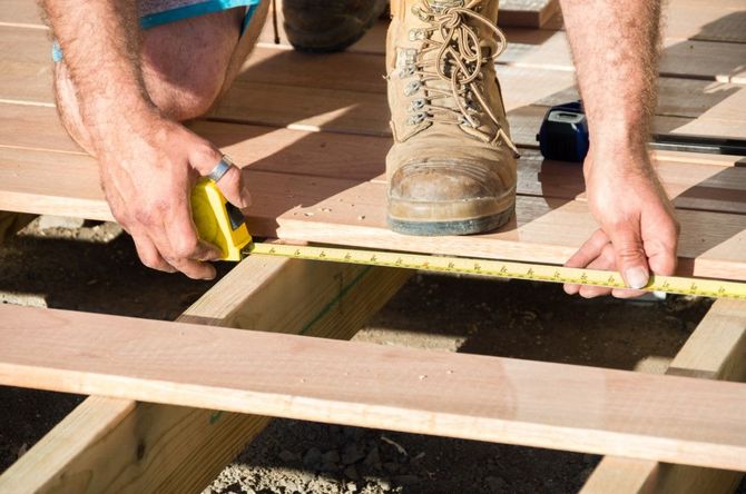 Measuring a wooden deck frame with a tape measure and utility knife