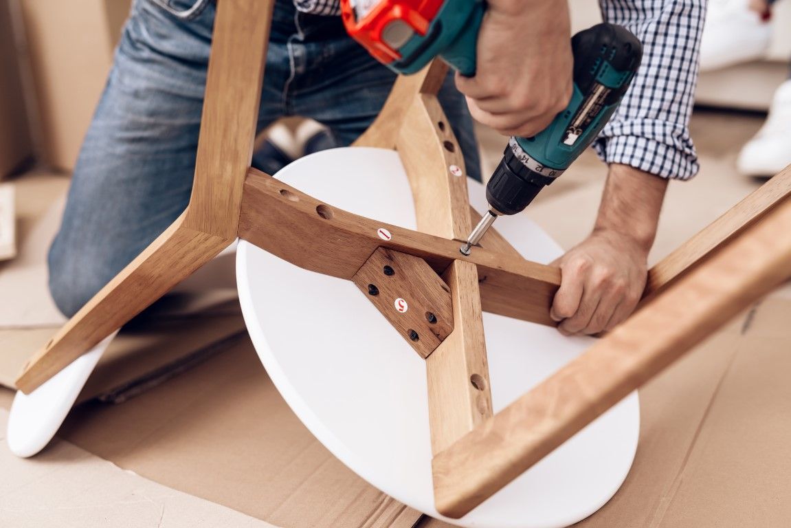 Person drilling a wooden chair frame with a white seat base attached