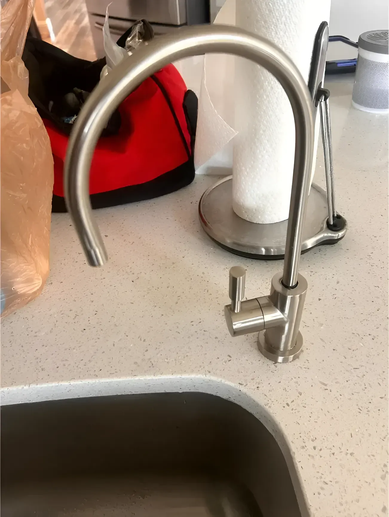 Brushed nickel faucet on a white countertop over a stainless steel sink, near a paper towel holder.