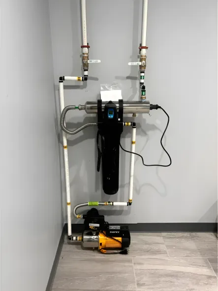 Water filtration system with a pump, pipes, and filter components mounted on a wall.