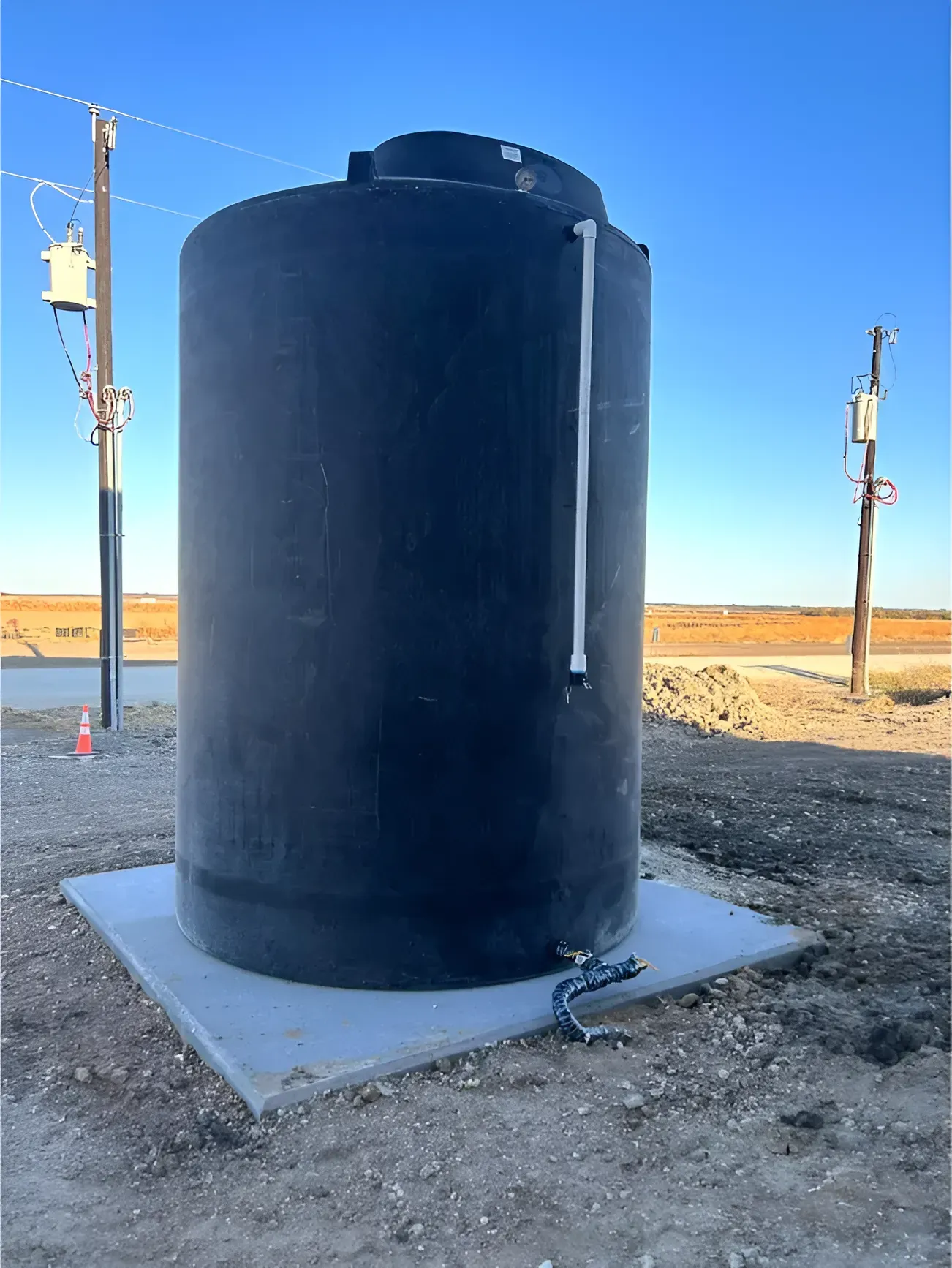 Black water storage tank on a concrete pad, outdoors, near power lines, clear sky.
