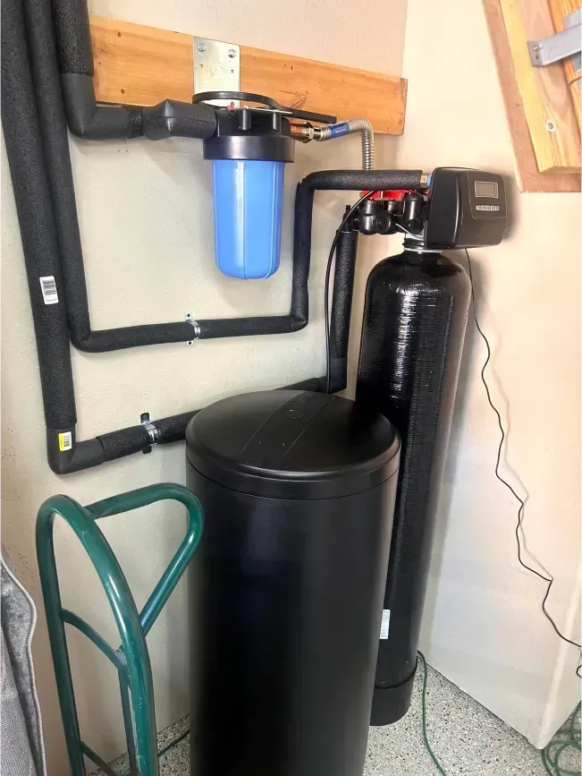 Water filtration system with black tanks, blue filter, and insulated pipes.