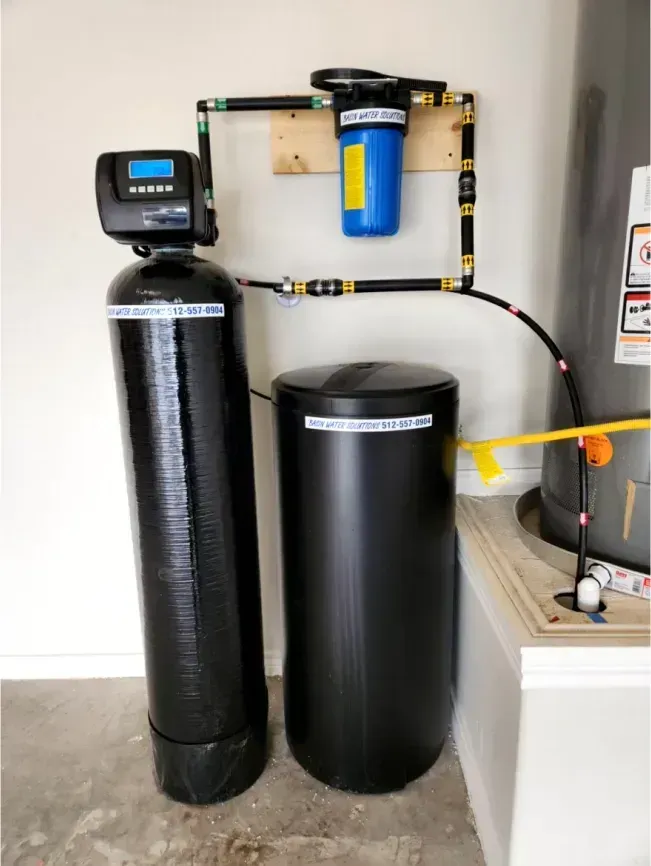 Water softener and filter system in a garage setting with blue filter housing and black tanks.