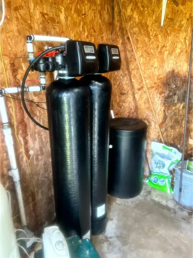 Water filtration system with two black tanks and a control unit, indoors.