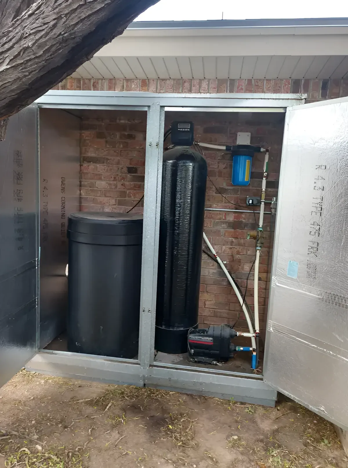 Water softener system in a metal enclosure. Contains a black tank, resin tank, filter, and a pump.