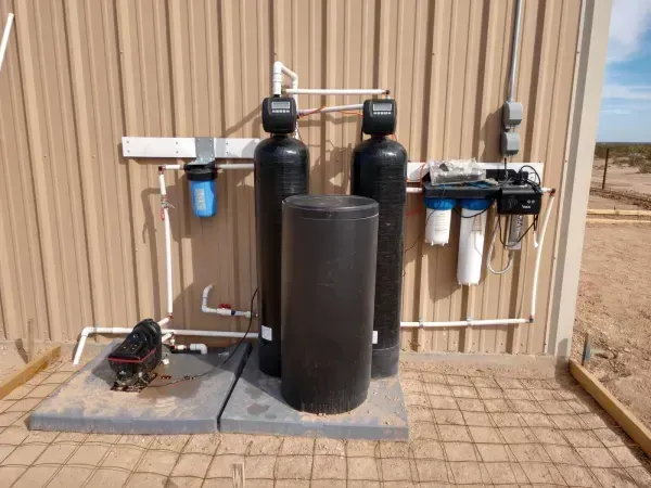 Water filtration system outside a building with two large black tanks, filters, and piping.