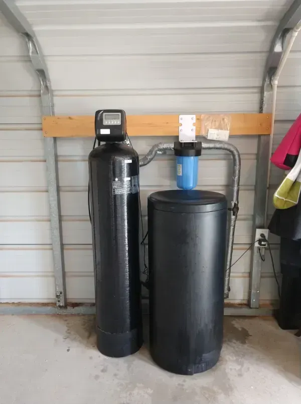 Water filtration system in a metal garage. Black tank, blue filter, and silver pipes.
