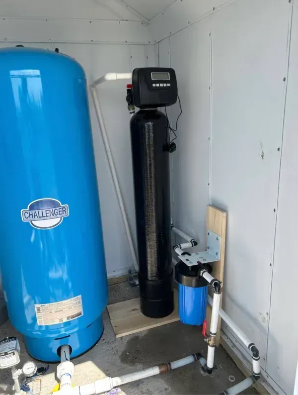 Water filtration system in a small white enclosure. Includes a blue pressure tank, black filter, and plumbing.