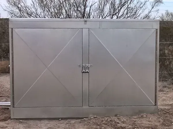 Metal utility box with two doors, padlocks, and diagonal design. Set outdoors on dirt.