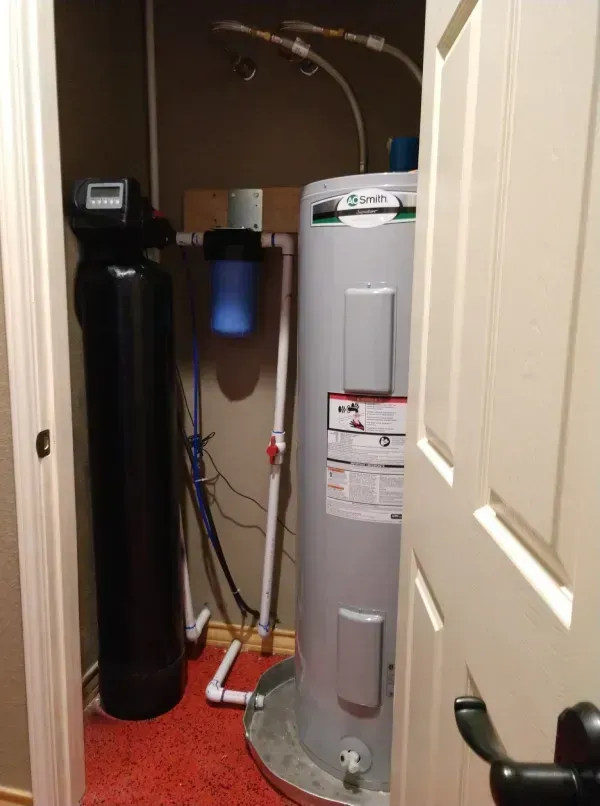 A water heater, filter, and water softener in a utility closet with a red floor.