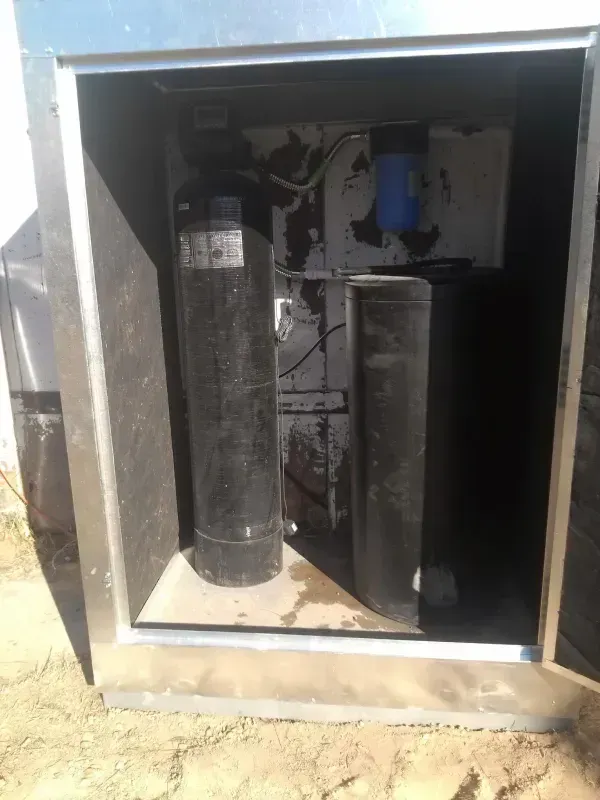 Water filtration system inside a silver enclosure; two black tanks, a blue filter, and wiring are visible.