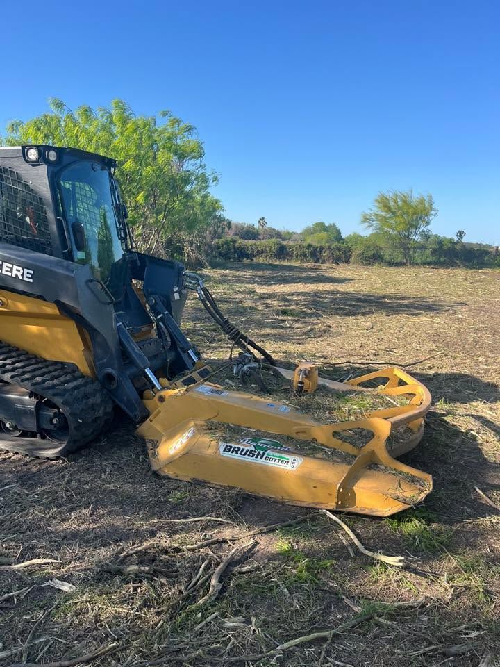 Yellow John Deere skid steer with a mulcher attachment clearing brush in a dry field under a blue sky