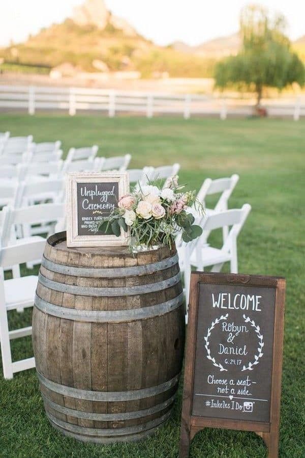 A wooden barrel sitting on top of a lush green field next to a welcome sign.