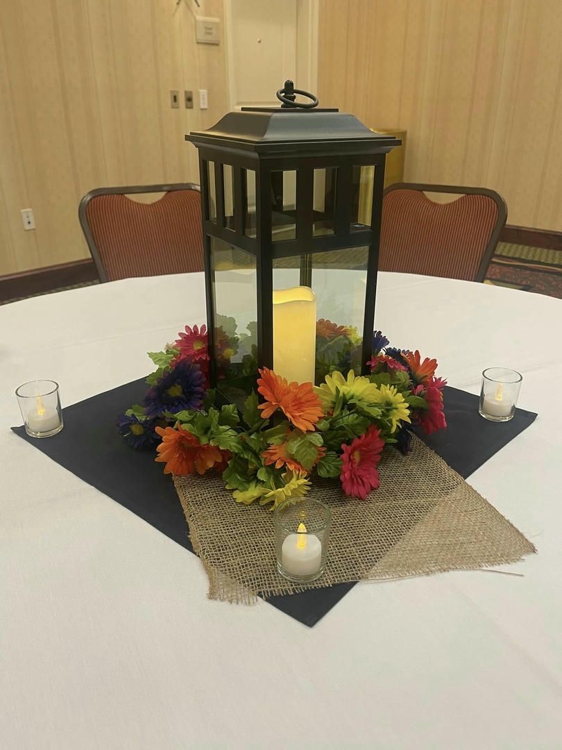 A lantern surrounded by flowers and candles on a table.