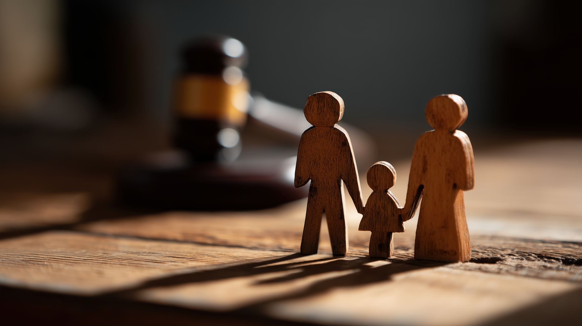 wooden figurines of two adults and one child holding hands on a wooden surface