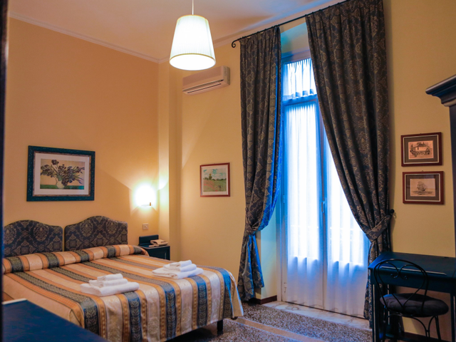 Camera da letto con letto, coperta a fantasia, finestra con tende scure, opere d'arte alle pareti e una lampada a sospensione.