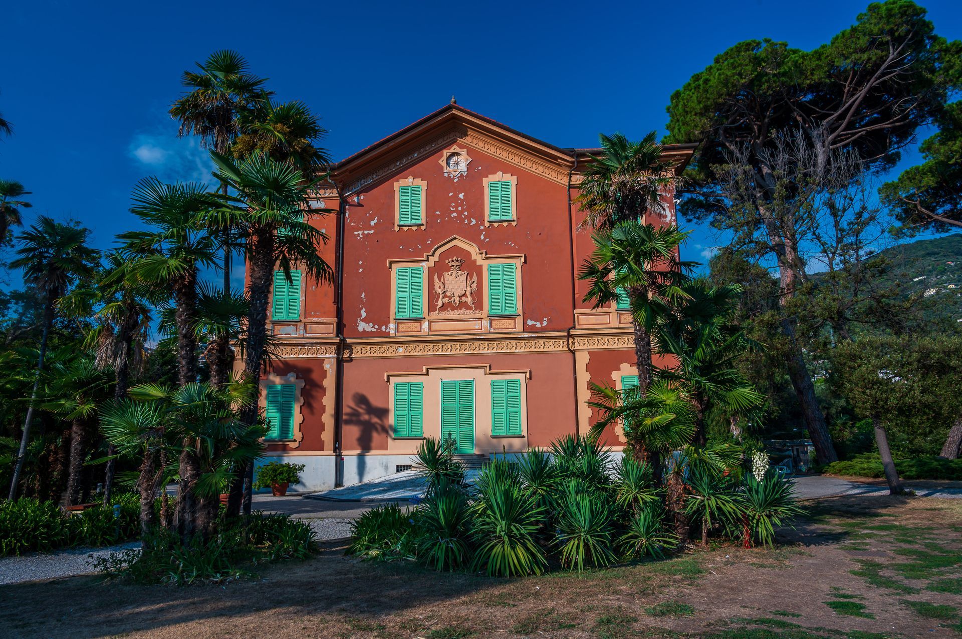 Edificio giallo con persiane verdi, balcone bianco e scale con ringhiera bianca contro il cielo azzurro.