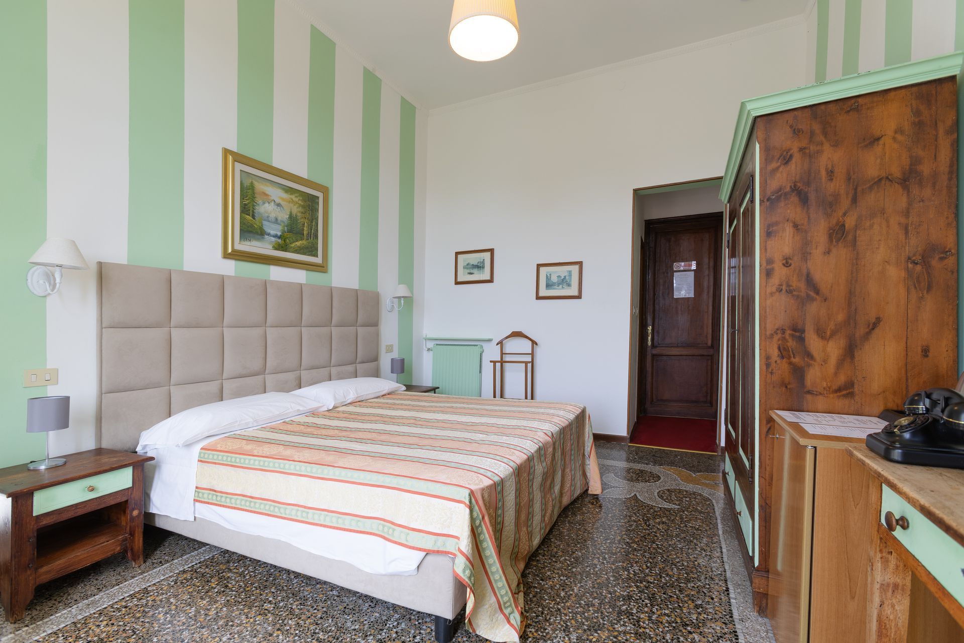 Camera d'albergo con pareti a strisce verdi e bianche, letto, armadio e telefono.