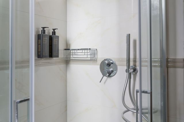 Doccia con porte in vetro, flaconi di shampoo su uno scaffale e accessori cromati.