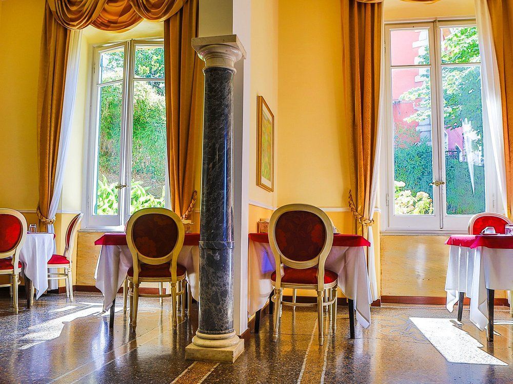 Elegante sala da pranzo con tavoli, sedie, finestre con tende e una colonna decorativa.