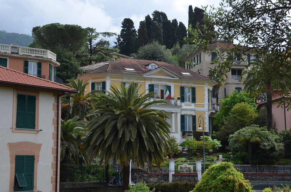 Villa gialla con bandiera italiana, palma e altri edifici, immersa nel verde.