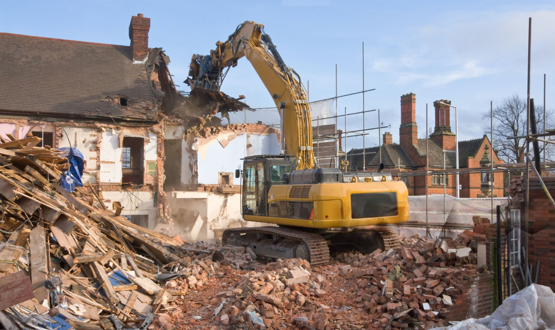 A large yellow excavator is demolishing a building