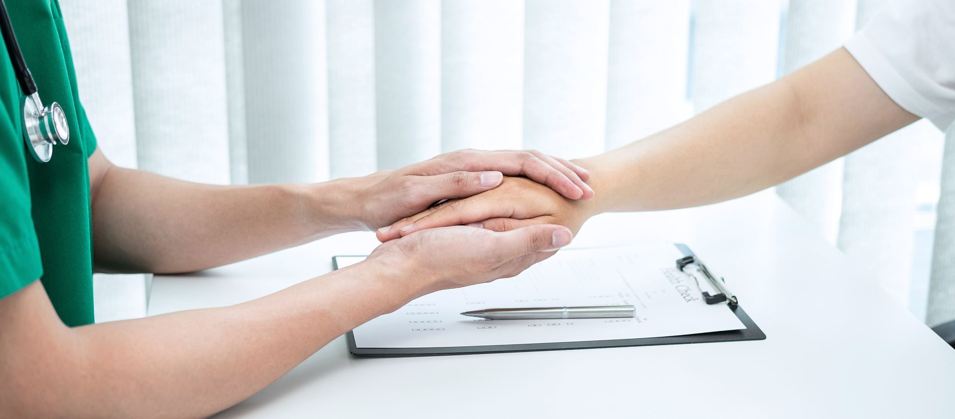 Closeup of the hands of a doctor holding a patient’s hands while conducting a medical exam.