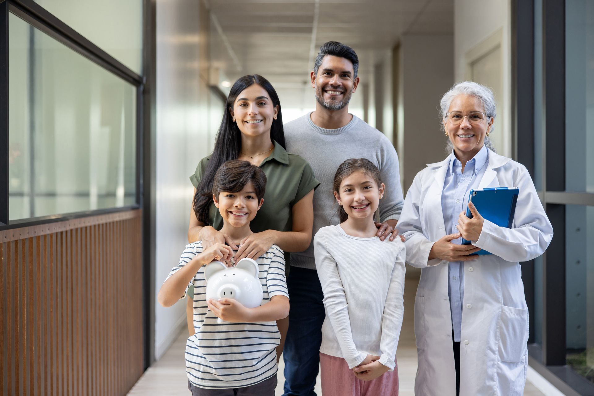 Doctor with family holding piggy bank, smiling together during a clinic visit.