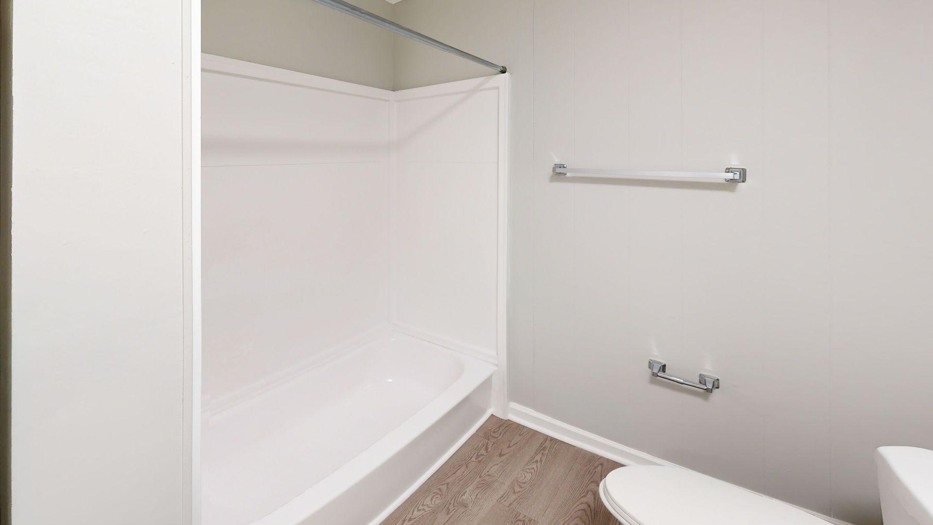 Empty white bathroom with a shower-tub combo, towel bars, and beige carpet flooring.