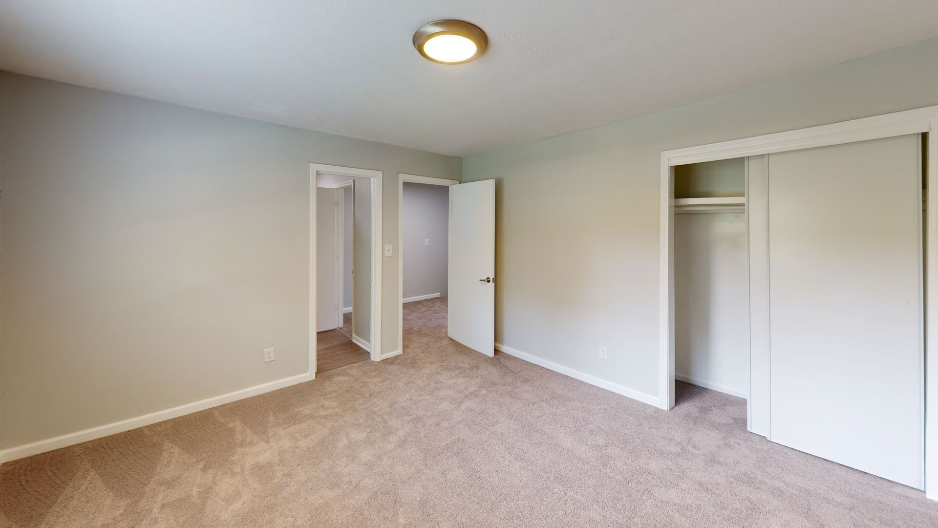Empty beige bedroom with carpet, two closets, and an open door leading to a bathroom or hallway