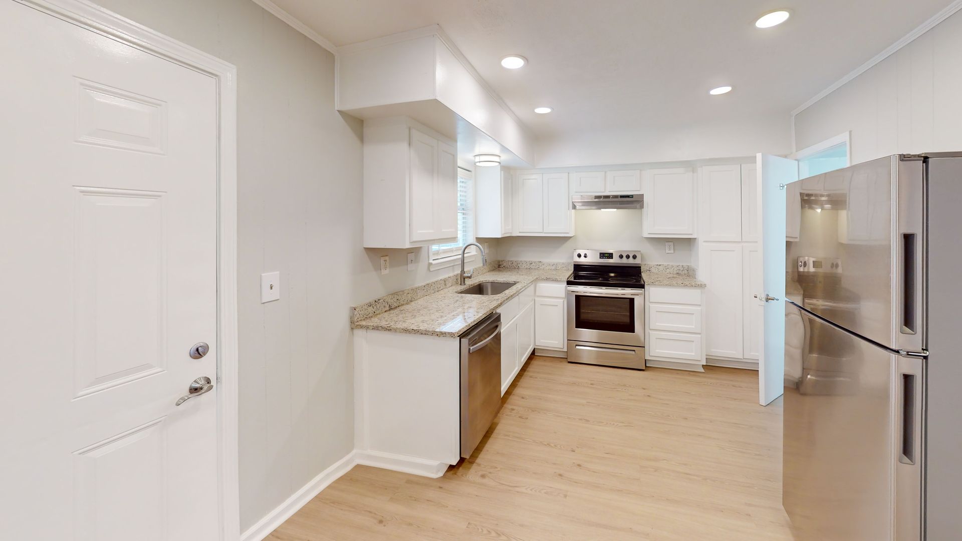 Bright modern kitchen with white cabinets, stainless steel appliances, and light wood flooring