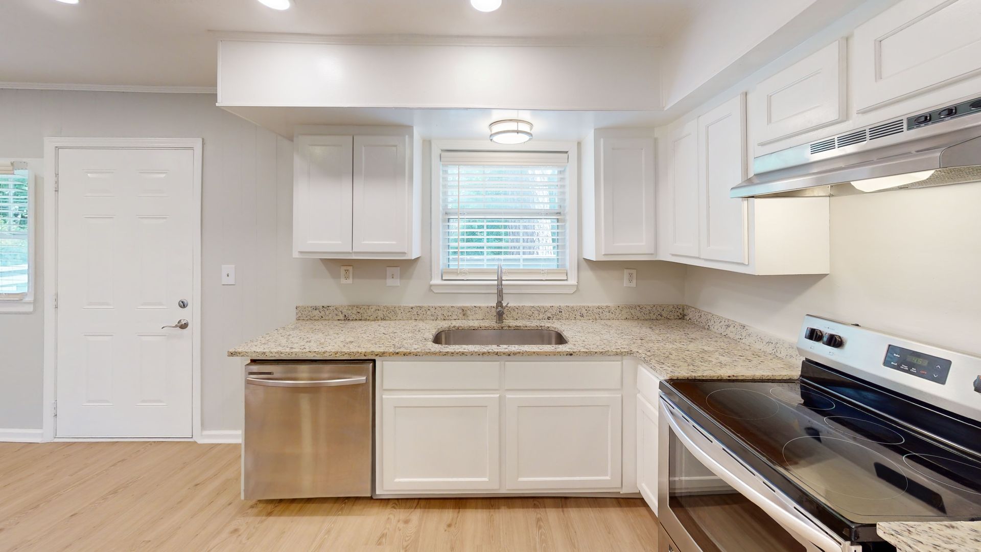Bright white kitchen with stainless steel appliances, white cabinets, and light wood flooring