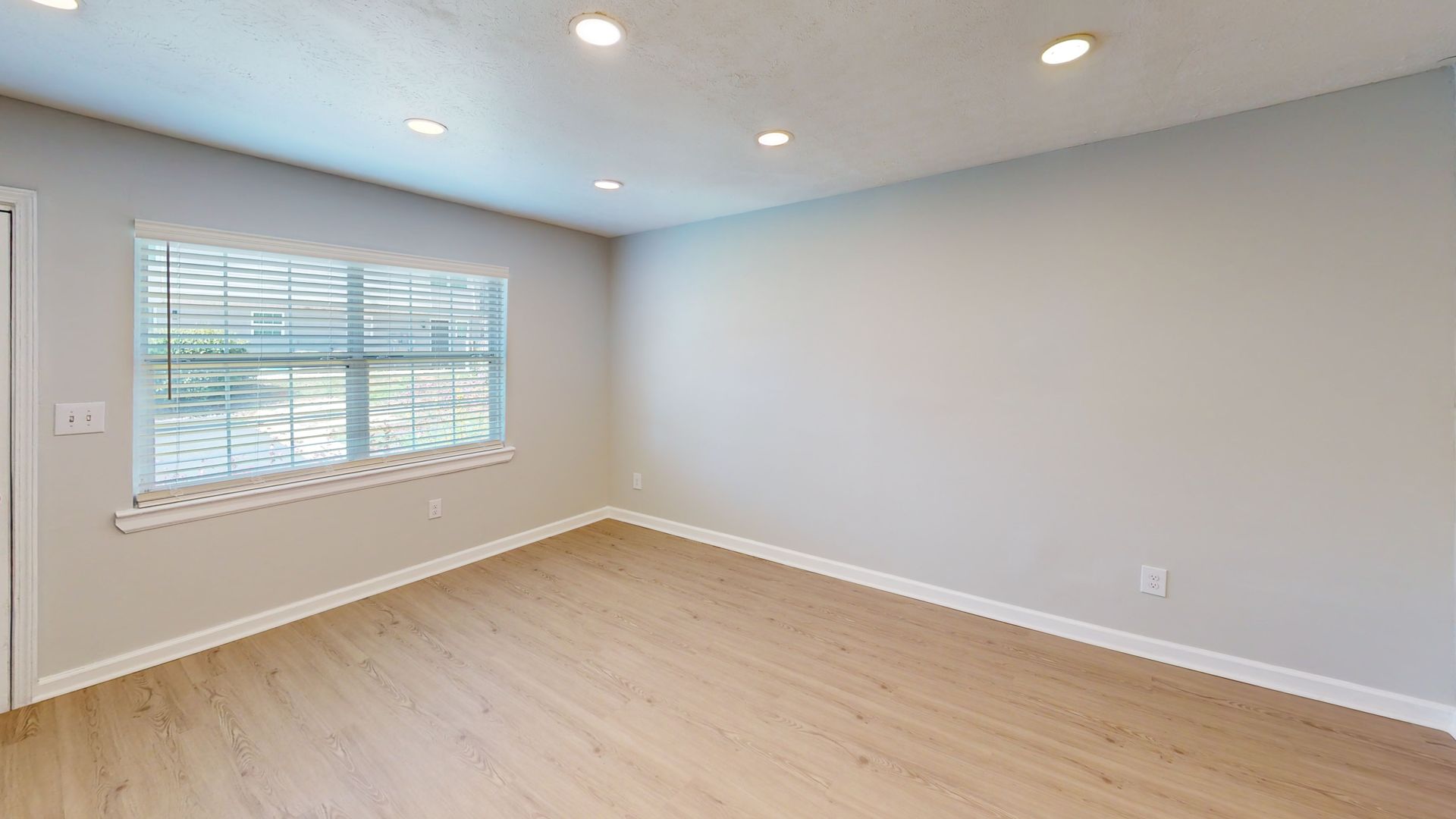 Empty light-gray bedroom with wood floors, window blinds, and recessed ceiling lights