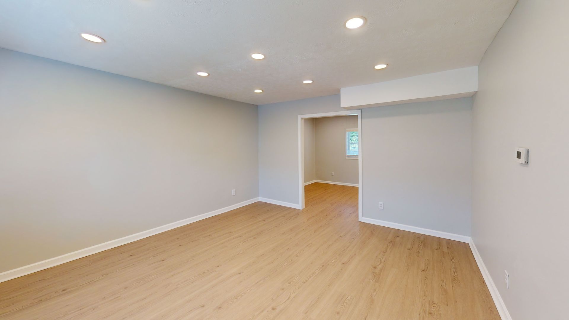 Empty modern room with light wood floors, gray walls, and recessed ceiling lights