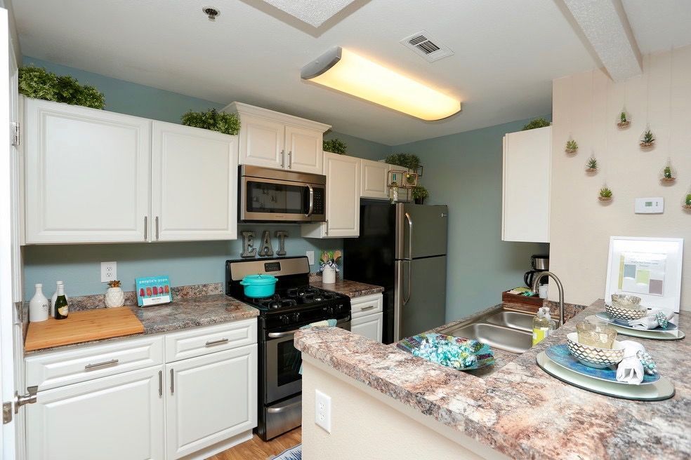 Bright white modern kitchen with stainless steel appliances, granite counters, and a large window.