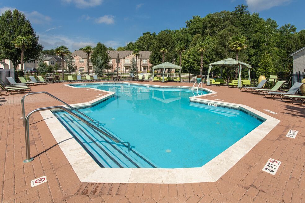 Outdoor swimming pool beside a two-story building with lounge chairs and trees in the background