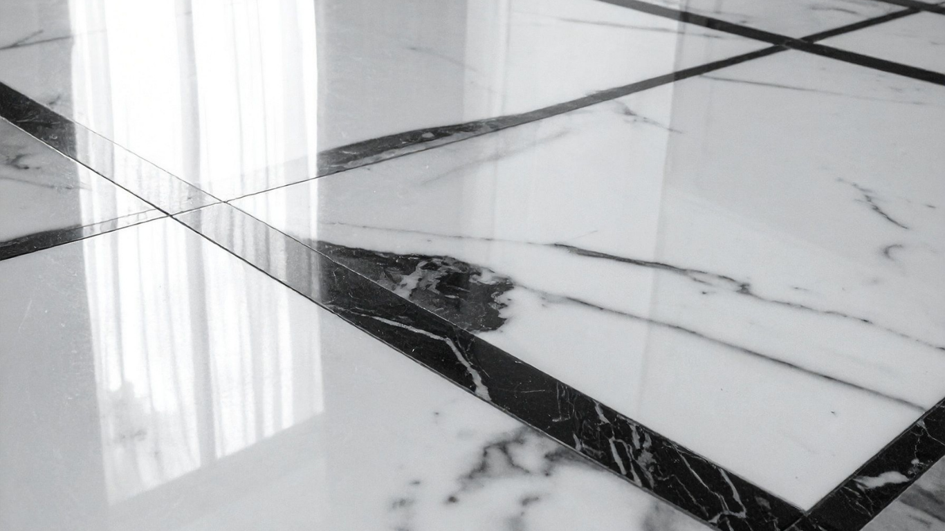 Close-up of polished white marble floor tiles with dark grey veins and thin black grout lines reflecting indoor light.