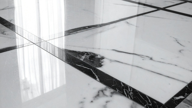 Close-up of polished white marble floor tiles featuring dramatic black veins and reflections of nearby curtains.
