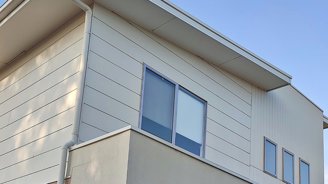 A low-angle view of a modern two-story building exterior with light-colored horizontal siding and a small balcony.