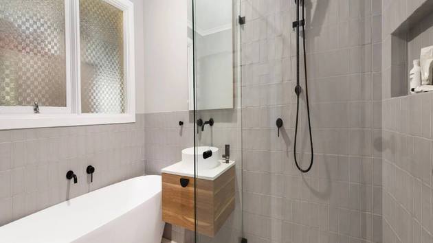 A modern bathroom featuring a white soaking tub, a floating wood-grain vanity, and a glass-enclosed shower with grey tiles.