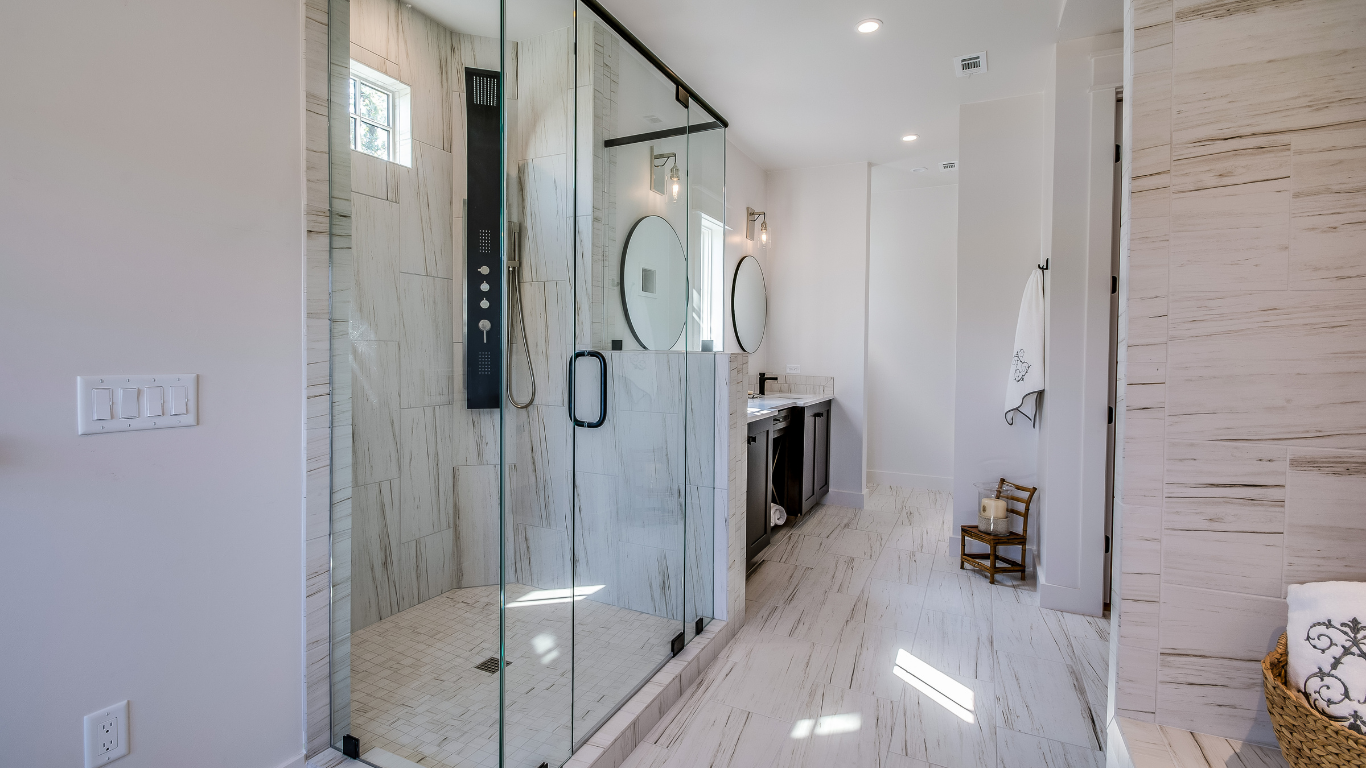 A modern bathroom with a glass-enclosed marble shower, light-colored tile floors, and a distant vanity.