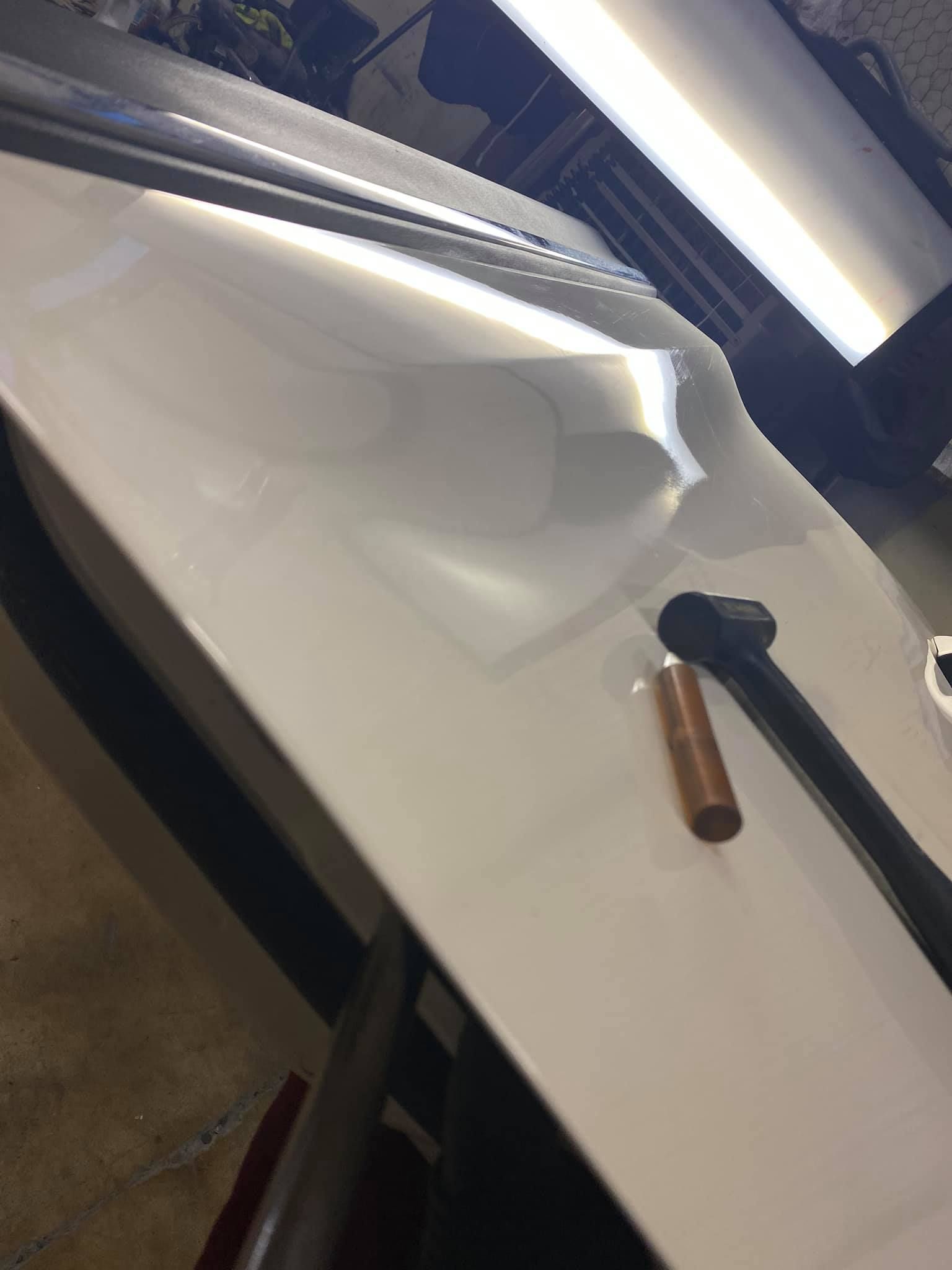 White car door with a large dent being worked on with tools.